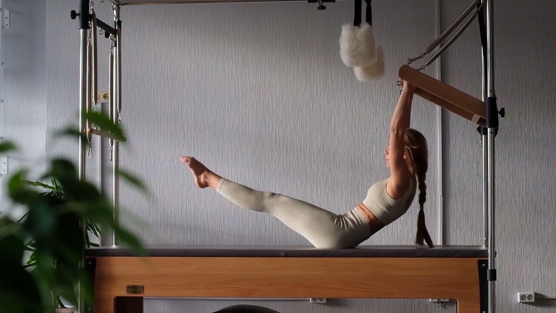 Woman on a Pilates Cadillac holding the push-through bar, legs raised